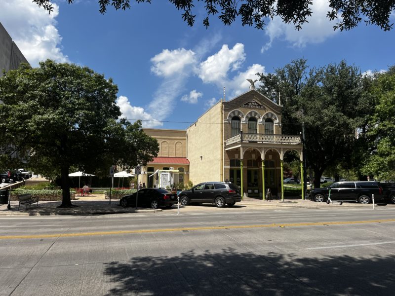 Photo of the outside of the old bakery emporiium building. It is a historic white building right across the street from the texas state capitol.